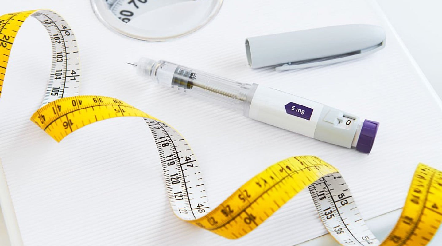 A weight loss injection pen resting on a tape measure and scales